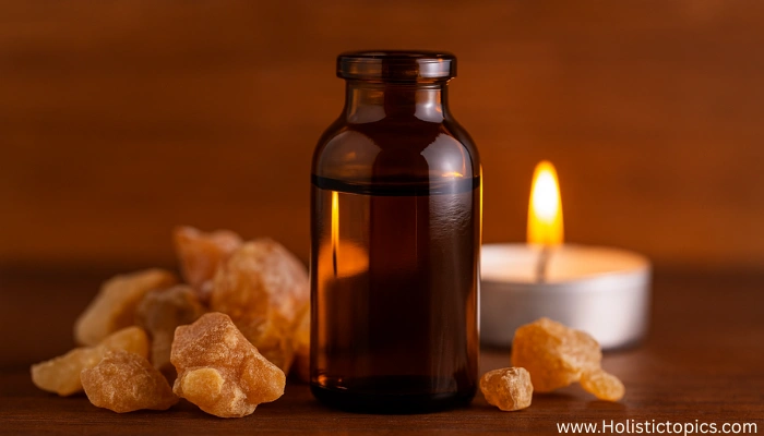 Amber bottle of frankincense essential oil surrounded by resin pieces and a warm candle, used in essential oils for energy cleansing practices