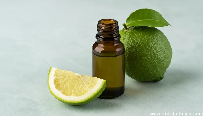 Amber glass bottle of bergamot essential oil with a whole bergamot fruit and a fresh citrus wedge on a soft green background.